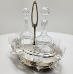 Conjunto de Licor Christofle com Duas Licoreiras em Cristal e Oito Cálices, França, c. 1880 a 1935 Refinado serviço de licor composto por duas licoreiras em cristal lapidado e oito cálices em cristal gravado, apresentados sobre estrutura fixa em metal prateado da prestigiada Maison Christofle. A base traz o tradicional carimbo C balança C, utilizado pela manufatura entre o final do século XIX e as primeiras décadas do século XX. As licoreiras, em cristal de grande transparência, possuem tampas facetadas esféricas e decoração gravada em ácido com guirlandas, típica da produção francesa frequentemente associada a fornecedores como Baccarat ou Saint-Louis. Os oito cálices acompanham o mesmo motivo ornamental, formando um conjunto inteiramente coerente e elegante. A estrutura metálica apresenta dois níveis suavemente arqueados para acomodação das taças e espaços centrais destinados às licoreiras, além de alça superior escultural de desenho alongado. Dimensões: 27 x 27 x 20 centímetros.