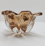 Elegante centro de mesa em vidro artístico. Peça modelada manualmente em forma orgânica de bordas onduladas. Vidro translúcido em tonalidade âmbar, executado com a técnica bullicante, na qual bolhas de ar são intencionalmente aprisionadas de modo regular, criando textura e luminosidade internas. Peça de composição fluida e brilho intenso. Dimensões: 8 x 17 x 17 centímetros