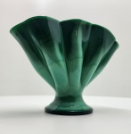Elegante vaso em vidro artístico soprado, com tonalidade verde intensa mesclada em nuances translúcidas, formando delicado efeito marmorizado semelhante à malaquita. De formato orgânico e ondulado, com abertura em leque e base circular, a peça apresenta proporções equilibradas e brilho vítreo notável. Dimensões: 20 x 26 x 9 centímetros.
