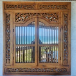 Espelho janela balinesa em madeira maciça, ricamente entalhada à mão. A moldura apresenta painéis laterais, barra superior e friso inferior trabalhados com motivos florais e folhagens sinuosas, em clássica linguagem ornamental da marcenaria tradicional de Bali.A parte central com folhas articuladas de gradeado vertical.Dimensões: 1,30x1,20 metros.