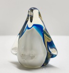 Peça decorativa em vidro artístico soprado, representando pinguim estilizado de linhas suaves e massa vítrea espessa, composta por corpo translúcido em tonalidade leitosa envolto por faixas trabalhadas em azul profundo e azul-claro, com sutis inclusões internas que evidenciam o processo manual de moldagem; figura de formato pleno e bem equilibrado, com volumes arredondados, asas insinuadas e cabeça levemente projetada, transmitindo equilíbrio formal e elegante simplicidade, típica da produção veneziana. Dimensões: 8 x 12 x 7 centímetros.