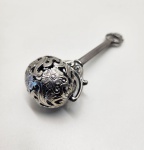 Raro infusor europeu de chá em metal prateado, ricamente elaborado, final do sec. XIX ao início do XX. A peça apresenta uma esfera vazada em delicado trabalho floral repuxado, com ramagens e pétalas em alto relevo, criando um efeito ornamental típico da ourivesaria artística do período vitoriano. O cabo alongado, de perfil facetado, incorpora uma bela argola decorativa na extremidade, equilibrando estética e funcionalidade. Dimensões: 13x5 centímetros.