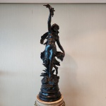 Escultura em petit bronze patinado, assinada Aug. Moreau na base assinatura de Auguste Moreau (18341917), escultor francês da escola romântica, reconhecido por suas figuras femininas graciosas e composições fluidas.A peça representa jovem figura feminina em movimento ascendente, com o corpo levemente arqueado e a mão direita erguida sustentando um pequeno arranjo floral ou raminho decorativo. A mão esquerda segura delicadamente o vestido, criando sensação de leveza e vento, elemento típico da modelagem dinâmica de Moreau.O traje esvoaçante, o cabelo solto e a base ornamentada com folhagens reforçam o estilo naturalista e ornamental característico do escultor. A obra se apoia sobre base circular em mármore. Dimensões:94 x 29 x 35 centímetros.