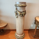 Imponente coluna decorativa confeccionada em terracota moldada, trabalhada em formato canelado de inspiração clássica. A peça apresenta acabamento patinado em tom marfim envelhecido, enfatizando o relevo suave das caneluras.Na porção superior, destaca-se uma guirlanda ornamental composta por flores, folhas e frutos em alto-relevo, com aplicação de douração envelhecida e nuances esverdeadas, criando contraste sofisticado e aparência de peça antiga.A base e a borda superior recebem friso decorativo com motivos vegetais, também realçados pela pátina dourada. Dimensões 1,30 x 0,41