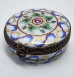 Encantadora caixa de porcelana Limoges Castel France, ricamente decorada com finos arabescos, guirlandas florais e delicados detalhes em ouro aplicados à mão. A superfície apresenta pintura refinada em tons suaves que ressaltam o brilho característico da porcelana de Limoges, enquanto o interior da tampa traz a inscrição dourada Délice de mon cur, adicionando um toque romântico e tradicional. As ferragens em bronze patinado mantêm o charme clássico das peças francesas, e a base exibe a marca Limoges Castel France acompanhada da etiqueta H. Stern, atestando procedência de alta qualidade. Dimensões: 2 x 6 centímetros.