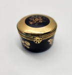 Caixa de porcelana Limoges Castel, marcada e distribuída pela H. Stern, decorada em esmalte azul-cobalto profundo com aplicações de ouro 22k. O corpo e a tampa exibem delicados ramos florais dourados, trabalhados com precisão e brilho impecável. A estrutura metálica apresenta fecho frontal em motivo floral, reforçando o acabamento luxuoso característico das peças produzidas em Limoges para joalherias de prestígio. Interior igualmente esmaltado em azul com detalhe floral pintado a ouro na tampa, demonstrando refinamento em todos os ângulos. Dimensões: 3 x 5 centímetros.