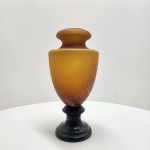 Vaso em pasta de vidro âmbar Europa, meados do século XX. Elegante vaso inteiramente executado em pasta de vidro (pâte de verre), com coloração âmbar em degradê e textura acidada. A base, igualmente em vidro, forma conjunto harmônico de proporções equilibradas e brilho difuso característico dessa técnica. Obra de grande presença decorativa, representando o refinamento da tradição europeia em vidro artístico. Dimensões: 37 x 18 centímetros.
