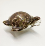 Delicada escultura zoomórfica em vidro artístico de Murano, modelada à mão na forma de tartaruga. Peça de corpo translúcido com inclusões metálicas em tons dourados e acobreados, criando efeito iridescente sob a luz. Trabalho típico das oficinas muranesas da segunda metade do século XX, de execução fluida e equilibrada, evidenciando a técnica do sommerso com uso de aventurina (partículas cintilantes de cobre). Dimensões: 6 x 13 x 12 centímetros.