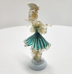 Escultura Pierrot em vidro artístico Murano, trabalhada à mão com aplicação de avventurina dourada no corpo e detalhes translúcidos em ouro-estrela. O personagem é modelado com o traje tradicional do Pierrot, exibindo saia em canas retorcidas verde-esmeralda e branco, típica das técnicas venezianas do século XX. A peça apresenta equilíbrio escultural, fluidez dos gestos e base em vidro opalino. Um trabalho decorativo de excelente efeito visual, representativo das oficinas de Murano da segunda metade do século XX. Dimensões: 21 x 10 x 8 centímetros.