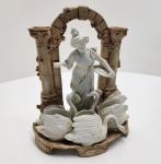 Peça em porcelana italiano, séc. XIX. Escultura representando jovem alimentando cisnes, modelada em biscuit branco sobre base com colunas e arco em tom ocre, evocando ruínas clássicas. O grupo apresenta três cisnes em alto-relevo ao redor da figura central, composição típica da produção decorativa italiana do período. Marca pintada a ouro na base. Trabalho harmonioso, de linhas suaves e acabamento delicado. Dimensões: 26   x 21 x 12 centímetros.