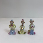 Conjunto composto por três pequenas esculturas de palhaços músicos, produzidas em porcelana policromada com detalhes dourados. As peças representam personagens musicais distintos, incluindo acordeonista e saxofonista, com acabamento esmaltado e rica pintura manual. Peças decorativas de estilo lúdico, típicas da tradição italiana de porcelanas figurativas inspiradas na escola Capodimonte. Medindo: