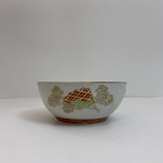 Tigela decorativa em porcelana oriental esmaltada, ricamente ornamentada com pintura policromada e detalhes em douração. A decoração interna apresenta figura feminina tradicional japonesa (geisha) em paisagem estilizada, acompanhada de leques e motivos florais. A borda é decorada com padrões florais e arabescos dourados, enquanto o exterior traz elementos de leques e flores em relevo esmaltado. Peça de caráter ornamental, típica da porcelana oriental decorativa.