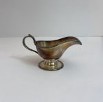 Molheira de mesa confeccionada em metal com banho de prata, apresentando bico vertedor alongado, alça lateral e base circular elevada. Interior com acabamento dourado e exterior com pátina natural de oxidação, característica comum em peças prateadas antigas.