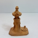 Escultura artesanal em terracota representando um oleiro trabalhando na roda de cerâmica, acompanhada de pequenos elementos da cena como utensílio e peças modeladas. A figura apresenta traços característicos da arte popular nordestina, com modelagem simples, expressiva e temática ligada ao cotidiano do sertão.