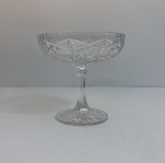 Fruteira em cristal lapidado incolor, com bojo amplo apoiado sobre haste e base circular. O corpo apresenta lapidação geométrica com estrelas, losangos e painéis facetados, criando forte efeito de brilho e refração da luz. Medindo: