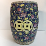 Banco decorativo em porcelana de estilo oriental, com fundo azul intenso e rica decoração floral policromada, incluindo borboletas e elementos naturais em composição detalhada.Apresenta aberturas laterais em formato de moedas chinesas, tradicionalmente associadas à prosperidade.