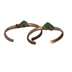 Duas pulseiras em metal prateado com pedras em formato de coração na cor verde.
