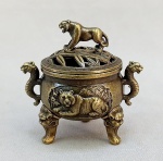 BRONZE, um (1) incensório com ornamentação relevada representando tigres, base trípode com patas saindo de dentro de carrancas, alças em S terminando em cabeça de tigre, tampa vazada em bambus, relevada em barrado grego, encimada por tigre, confeccionado em bronze, medindo aproximadamente 5,5 cm altura, vide foto.