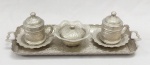 METAL PRATEADO TURCO, conjunto tete a tete para café com quatro (4) itens: 1 bandeja; 1 açucareiro e 2 xícaras com tampa, parte interna em vasilhames de porcelana com facetados octogonais quase cilíndricos  na tonalidade branca, arremates com frisos prateados, ornamentação relevada no padrão Império Otomano com elementos vegetalistas e geometrizados, marca de origem em relevo na bandeja, medindo a maior peça 36 cm comprimento, não aparenta ter sido usada ou pouco uso, vide foto.