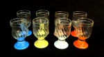 VIDRO, oito (8) taças de pé baixo, bojo incolor e translúcido, moldado em caneluras espiraladas, fuste cilíndrico e base na forma de saia em cores variadas, medindo 12 cm altura, sinais de uso, vide foto.