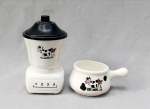 FAIANÇA, dois (2) itens distintos, ambos ornados com motivos de vaca holandesa em policromia e sem marca de manufatura aparente: 1 pote modelado na forma de liquidificador, tampa em polímero, medindo 21 cm altura; 1 panela, medindo 12,5 cm diâmetro mais o cabo, ambos os itens com sinais de uso, vide foto.
