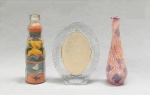 VIDRO, três (3) itens, incolores e translúcidos: 1 garrafa reaproveitada para escultura em areia colorida, arte popular representando barcos, peixes, pássaros e elementos vegetalistas, medindo 17 cm altura; 1 porta-retratos, oval, parte de traz com modelagem geometrizada, medindo 16 cm altura; 1 vaso solifleur, recoberto com decalque policromado com predominância da tonalidade rosa, medindo 17 cm altura, todos os itens com sinais de uso, vide foto.