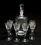 DEMI CRISTAL, conjunto com sete (7) itens, incolores e translúcidos: 1 licoreira com tampa, medindo 26 cm altura; 6 taças de pé alto com bojo obcônico, fuste cilíndrico, base em bolacha, medindo 12 cm altura, todos os itens lapidados em sulcos e estrelas, tampa facetada, sinais de uso, vide foto.