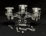 VIDRO, um (1) candelabro para três lumes, incolor e translúcido, modelagem terminando em volutas, traz três bobeches soltas ornadas com penduricalhos facetados (alguns soltos, outros faltando), medindo 19 x 32 x 9 cm, sinais de uso, vide foto.