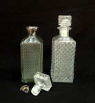 VIDRO, duas (2) licoreiras retangulares com tampa e distintas, incolores e translúcidas, ambas modeladas no padrão bico de jaca, uma delas com gargalo quebrado, medindo em média 25 cm altura, sinais de uso, vide foto.