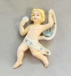 BISCUIT, um (1) adorno de parede representando anjo segurando buque de flores, envolto em faixa, policromado, medindo 13 cm altura, vide foto.