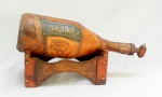 BEBIDA, uma (1) garrafa de cachaça vazia, recoberta em couro, torneira na extremidade, base expositora em madeira e couro, ideal para decoração de bar, medindo 39 cm, vide foto.