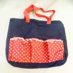 ACESSÓRIO FEMININO, uma (1) bolsa factory, confeccionada em tecido brim na tonalidade azul, detalhes de tecido vermelho com poás brancos, adornada com pompons brancos, fechamento em zíper, acolchoada, alças em gorgorão vermelho, formando bolsos, medindo 40 x 38 x 8,5 cm, vide foto, usada.