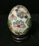 Antigo Ovo em closoinné sobre peanha com fundo branco e decoração em florais multicolorido,com suporte de madeira. Alt. 65mm