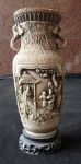 Vaso chinoiserie em marfinite, muito bem trabalhado com cenas de guerreiros orientais palacianos, alças no formato de cabeça de elefante. Alt. 30 cm." Chinoiserie é um estilo decorativo e artístico europeu do século XVII e XVIII que imita e interpreta a arte e a cultura chinesa, com elementos como dragões, pagodes, flores exóticas e cenas fantásticas, resultando em um visual ornamentado, elegante e exótico, popularizado no Rococó. Não é uma cópia autêntica, mas uma visão ocidentalizada do Oriente, usada em móveis, cerâmicas, tecidos e pinturas.  "