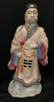 Escultura porcelana oriental, ancião com cajado representando divindade chinesa, como Deus  da Riqueza (Caishen) , rica policromia e detalhada representa figura masculina com barba  longa, fio de cabelo na base, vestido com o manto do Dragão, sendo item de colecionador e muito utilizada em decoração, podendo datar do período republicano .chinês (1912-1949) ou de época posteriores. Com altura de 28 cm.xxxx Obs:. Estas informações são baseadas em descrições gerais de itens semelhantes encontrados em leilões e lojas de antiguidades e não constituem uma avaliação ou certificação profissional da peça específica na imagem.