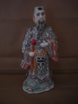 Escultura porcelana oriental, ancião com cajado representando divindade chinesa, como Deus  da Riqueza (Caishen) , rica policromia e detalhada representa figura masculina com barba  longa, fio de cabelo na base, vestido com o manto do Dragão, sendo item de colecionador e muito utilizada em decoração, podendo datar do período republicano .chinês (1912-1949) ou de época posteriores. Com altura de 28 cm.xxxx Obs:. Estas informações são baseadas em descrições gerais de itens semelhantes encontrados em leilões e lojas de antiguidades e não constituem uma avaliação ou certificação profissional da peça específica na imagem.
