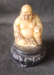 Escultura de Buda em marfinite sob peanha de resina preta. Alt. 10cm