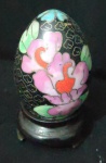 Magnifico Ovo de Cloisonnèe decoração de florais com fundo preto e base de peanha de madeira , O ovo apresenta um design complexo de flores rosa e folhas verdes sobre um fundo escuro, com detalhes em metal visíveis.. com alt total de 80mm.