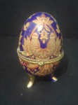 Caixa porta joia de porcelana colorida na forma de ovo, decorada com flores e personagens, guarnição de metal. Alt. 9,5cm
