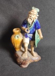 ARTE ORIENTAL - Escultura em cerâmica vitrificada de Mud-man, figura de ancião  com cesto segurando chapéu. Med. 12 cm altura.
