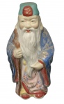 Estatueta de porcelana oriental, provavelmente chinesa ou japonesa, representando um monge ou sábio, como Fukurokuju, o deus da longevidade e sabedoria na mitologia japonesa. A peça é feita de porcelana esmaltada e vitrificada, com policromia e, às vezes, detalhes em ouro. Alt. 11