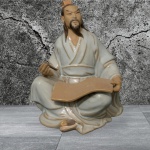 Estatueta de cerâmica chinesa, provavelmente uma figura de "mudman" de Shiwan, que representa um sábio ou mestre oriental sentado. A figura é feita de cerâmica vitrificada com detalhes pintados à mão. É um exemplo do estilo de cerâmica tradicional de Shiwan, conhecido por suas expressões detalhadas, escriba oriental com pequena perda do lápis na mão, tonalidade azul e marrom. Med. 13cm x 11 cm x 8,5cm