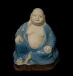 Estatueta de Buda Sorridente (Hotei), uma figura chinesa reverenciada como símbolo de sorte, felicidade, fartura e riqueza interior. A peça é uma escultura de porcelana com detalhes em esmalte azul. O Buda sorridente é frequentemente confundido com Siddhartha Gautama, mas é uma figura distinta que representa a benevolência e a alegria.  Com 9,5 cm de altura