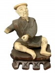 Escultura de bronze cor marfim de camponês sentado  sobre base de madeira. com 11 cm de altura