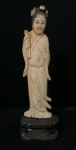 Eestatueta antiga cor marfim entalhado representando uma figura oriental, como uma gueixa ou divindade,  montada sobre uma base de madeira de origem chinesa ou japonesa, datando do século XIX ou início do XX. Com detalhe  segurando elementos como flores de lótus, leques ou ramos.
