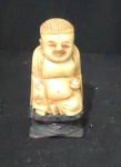 Netsuke cor marfim, figura de Buda sobre base de madeira. Alt total 75mm