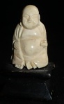 Okimono escultura oriental representando Buda, não possui assinatura, confeccionado na cor  marfim com base em madeira, medindo a escultura 3,5cm de altura, a base 1,5cm de altura