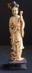 Figura esculpida cor marfim, representando deusa oriental segurando flor de lótus aberta na mão direita e botão de flor de lótus na mão esquerda, com policromia nos cabelos e base em madeira pintada na cor negra. Excelente estado, 17,5 cm de altura