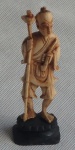 Imponente escultura cor marfim, sob pedestal de madeira, representando homem com cajado. Medindo 13cm