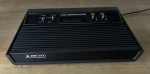 ATARI 2600 versão americana original, fábrica de El Paso. FUNCIONANDO no momento, sem garantia futura. Acompanha fonte genérica - Para solicitação de mídias adicionais e esclarecimento de dúvidas, entrar em contato através do telefone (21) 99377-0652 ----- Trata-se de um modelo "híbrido" entre o Woodgrain e o Darth Vader. Ele tem a moldura laranja ao redor do painel de chaves (como o Woodgrain), mas o painel frontal é totalmente preto com o nome e o logotipo da Atari 2600 impressos em branco (como o Darth Vader).Possui um número de série com um sufixo (EP-054) que, significa que foi fabricado em El Paso, Texas, na 5ª semana de 1984. Essa fábrica produziu uma série de consoles para  fins promocionais/de demonstração, provavelmente aproveitando peças existentes no estoque dos dois modelos de console.Uma curiosidade: A fábrica de El Paso também foi o local de origem dos cartuchos do famoso jogo do ET nunca vendidos que foram misteriosamente levados em um comboio de caminhões e enterrados no deserto de Alamogordo, no Novo México, a quase duas horas de distância. Essa lenda urbana foi confirmada/esclarecida em uma expedição de escavação em 2014, quando 1.300 cartuchos foram desenterrados e documentados em vídeo disponível na Netflix.